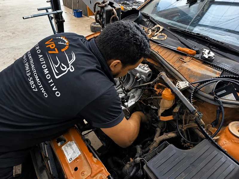 Mecânico da VP7, com a camisa da oficina, trabalhando no motor de um carro com o capô aberto
